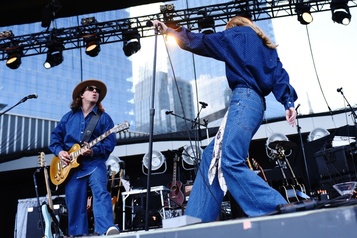 A blond woman wearing blue performs on stage while her guitarist wears matching clothes.