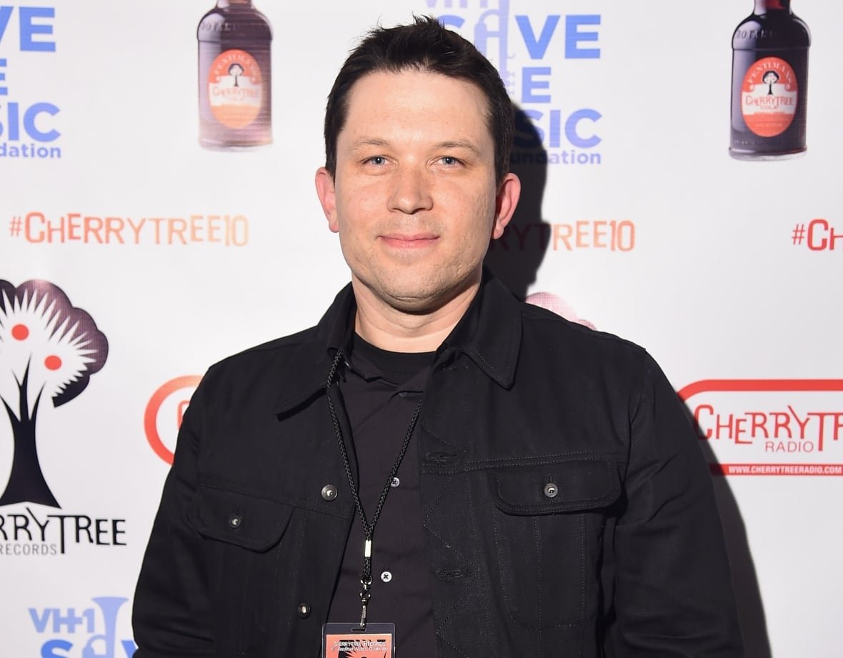A man with black hair is shown dressed in black.