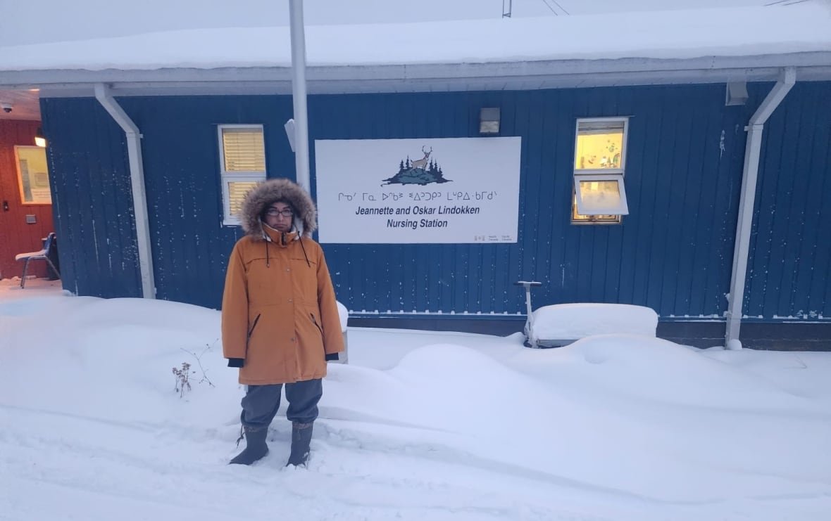 amanda-meekis A person stands in the snow outside of a blue-coloured building.