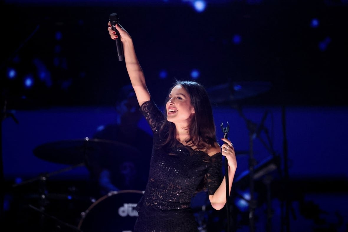 A young woman smiles on a stage and holds up a microphone.