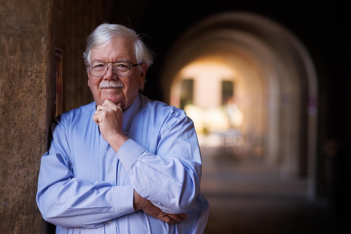 henry-greely A man with white hair, glasses and a blue button up shirt poses for a professional head shot photo.