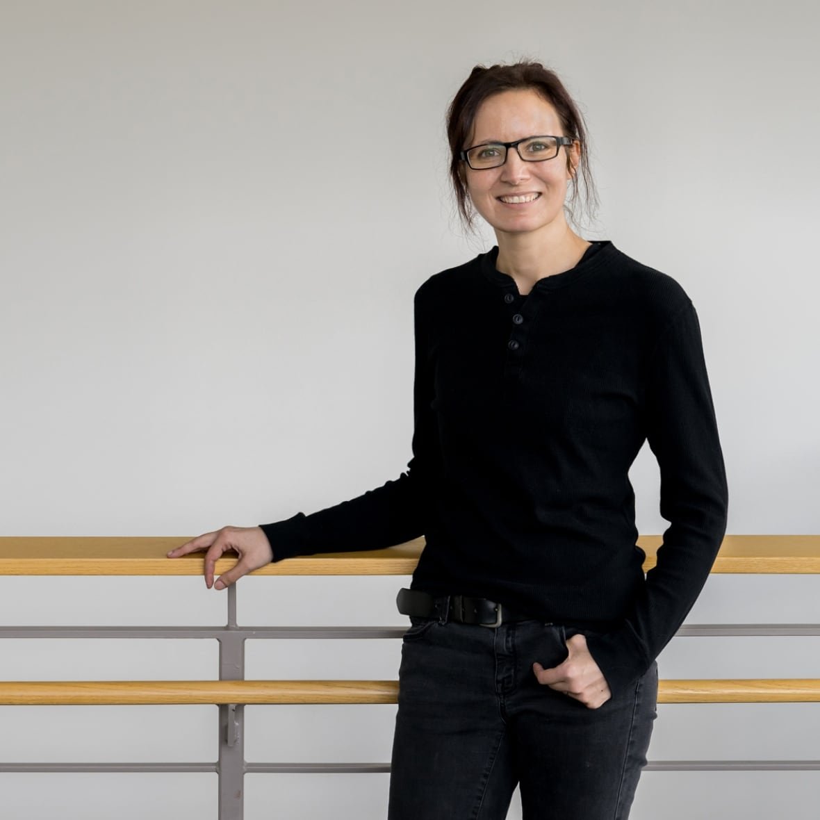 kate-adamala A woman with glasses and a dark long sleeve shirt smiles for a professional headshot photo