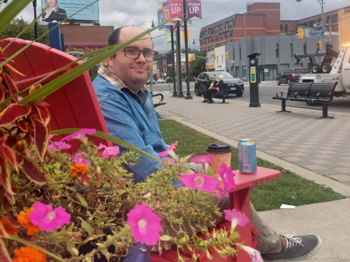 sam-dunsiger-flowers A man sits on a red chair near flowers.