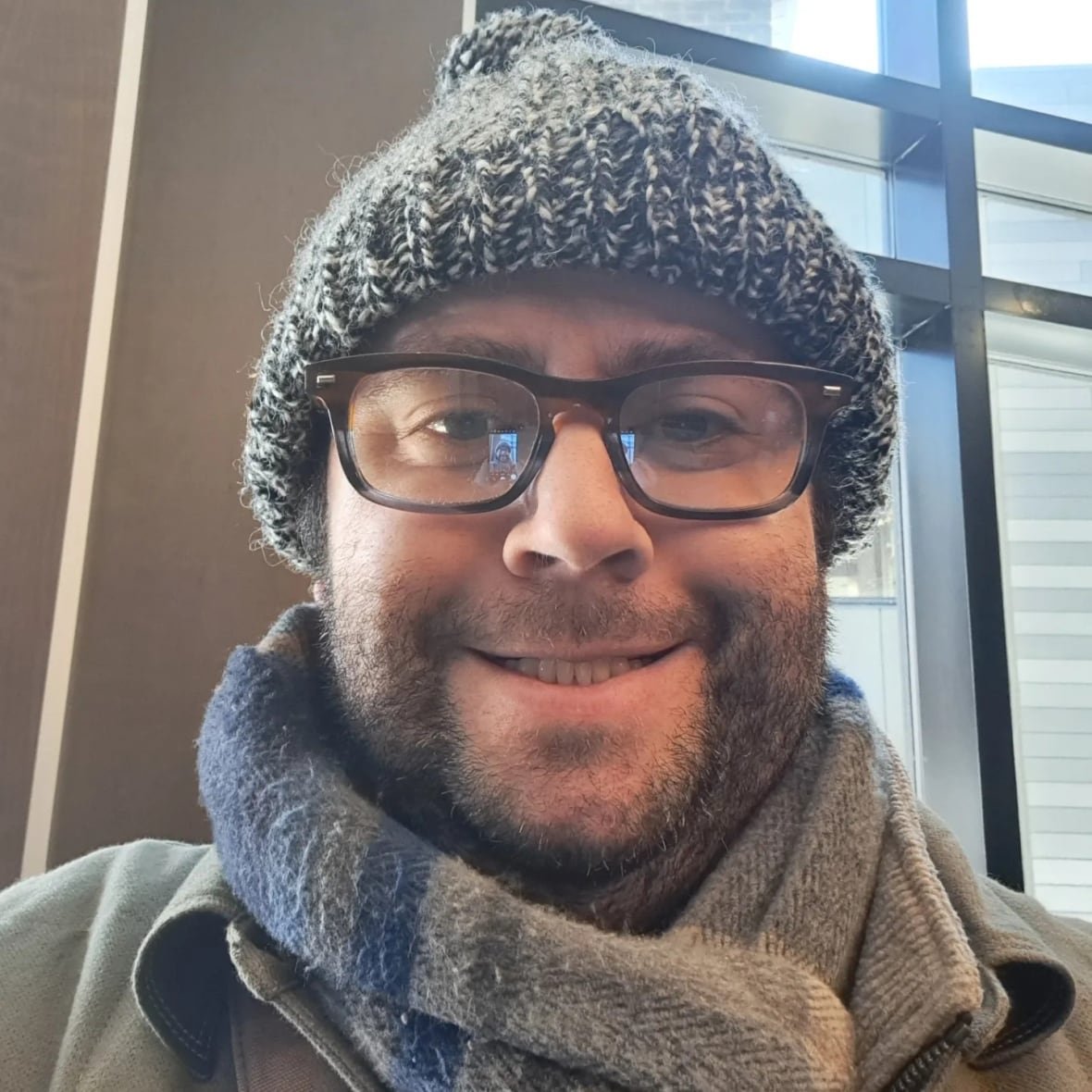 sam-dunsiger-head-shot A man with a beard, glasses and a winter hat smiles for the camera.