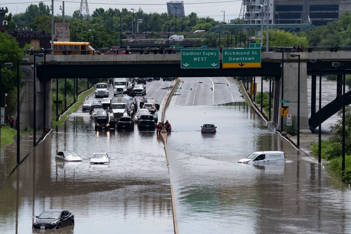 toronto-dvp-flooding Several cars are seen partially submerged in water on a roadway, with traffic stopped ahead of the water.