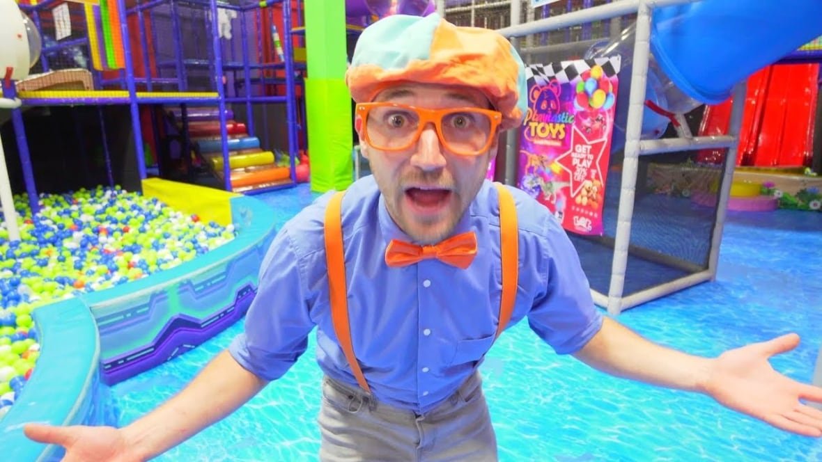 blippi A man in a colourful hat and costume stands in an indoor playground.