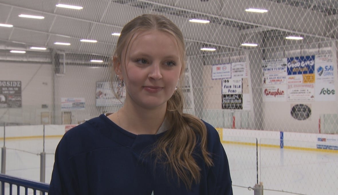 Girl with ponytail stands in ice hockey arena in the stands.
