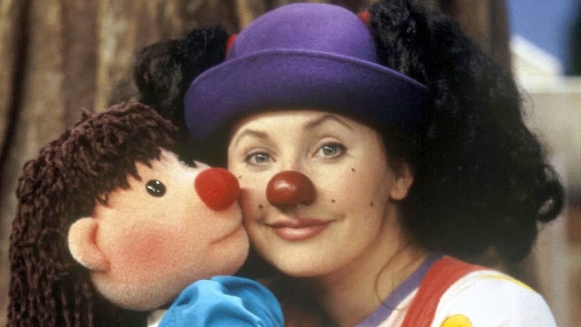 loonette A woman wearing a clown nose and a purple hat snuggles up to a doll puppet