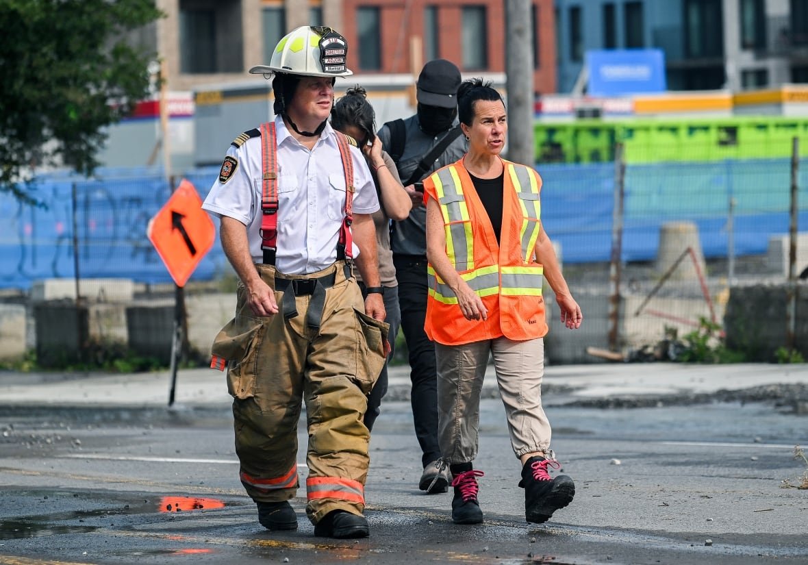 A woman wearing a security vest and boots walks next to a fire chief.