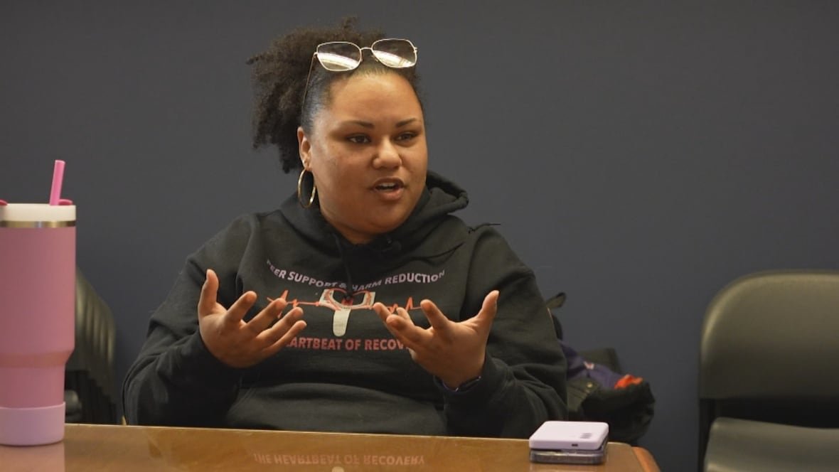 aaliyah A woman in a hoodie is pictured sitting at a table speaking.