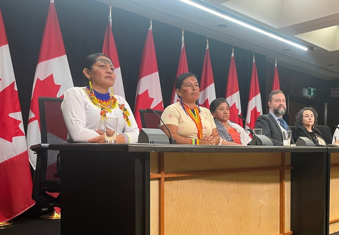 amnesy-ecuador People are seated at a press conference with Canadian flags behind them.
