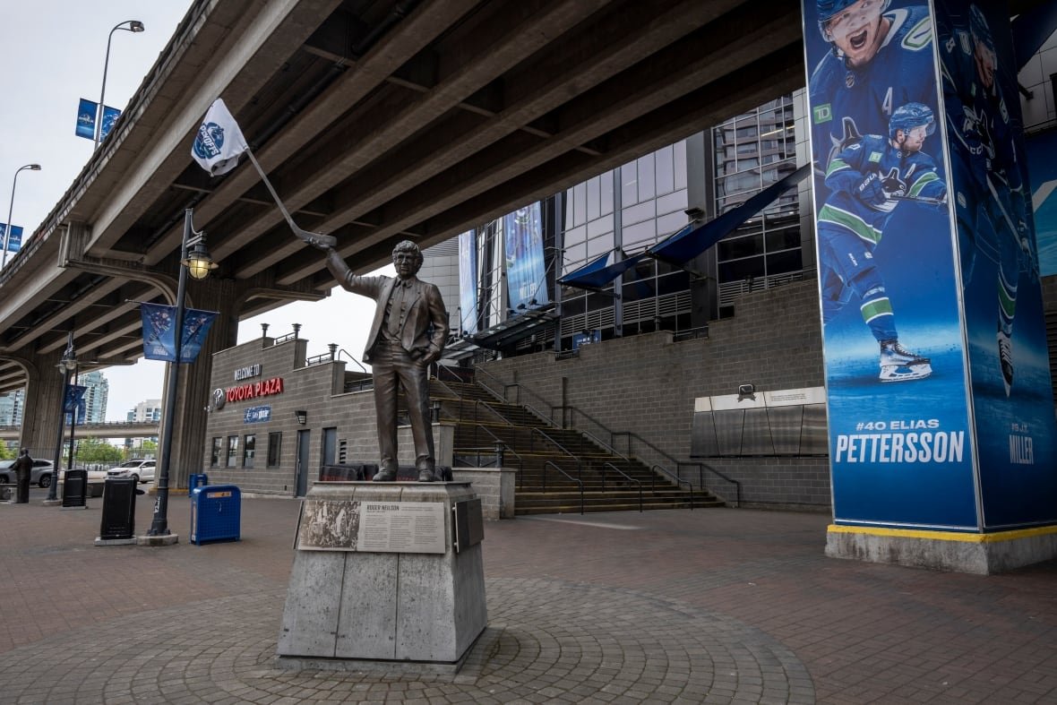 aritst-hub-825-pacific-roger-neilson A statue of a man waving a white flag is seen underneath an expressway and a stadium banner.