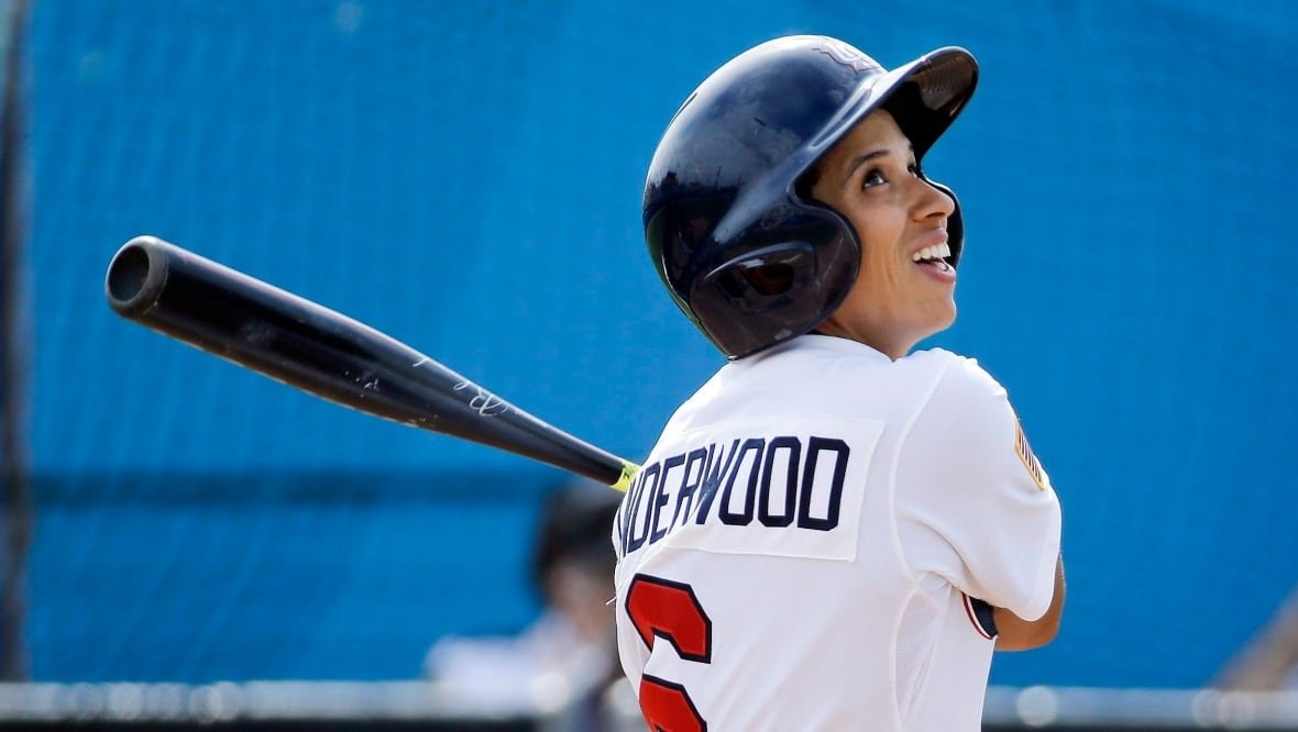 A female baseball player is pictured at bat.