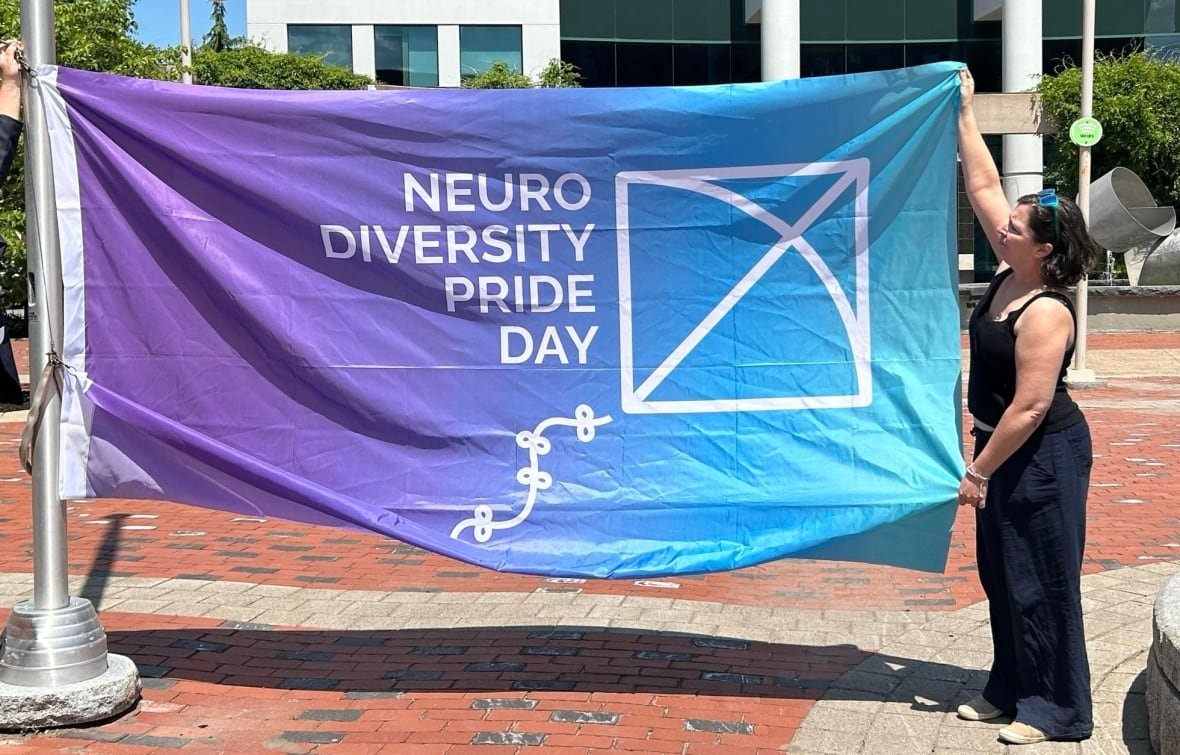 caroline-jose-neurodiversity-pride-day-flag A woman holds up a large purple and blue flag.