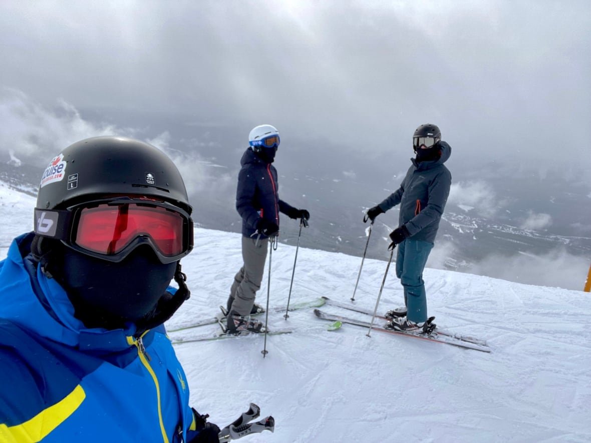 dejan-ratkov Three people in snowsuits and ski goggles standing on a snowy ski hill.