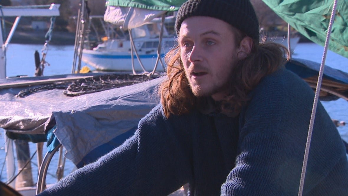 false-creek-boats A long-haired man in a blue tuque and sweater sits on his boat moored beside another boat.