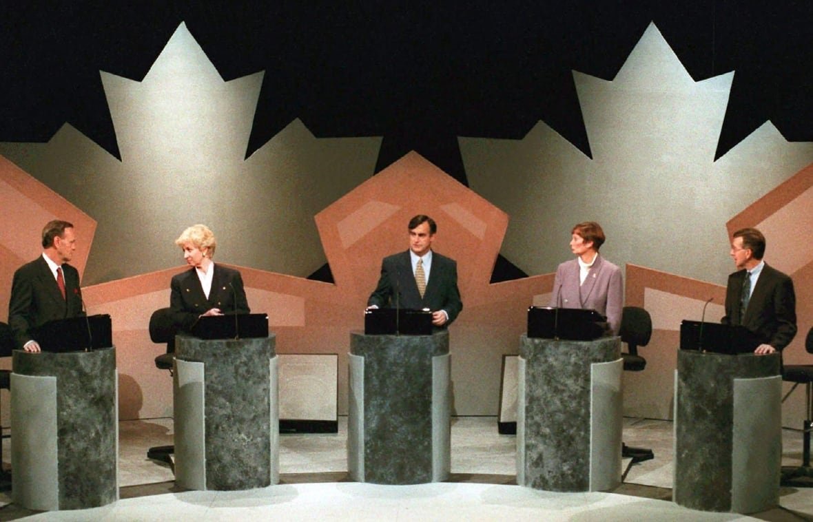 fedelxn-debates The leaders stand at podiums, behind them are large maple leaf decals.