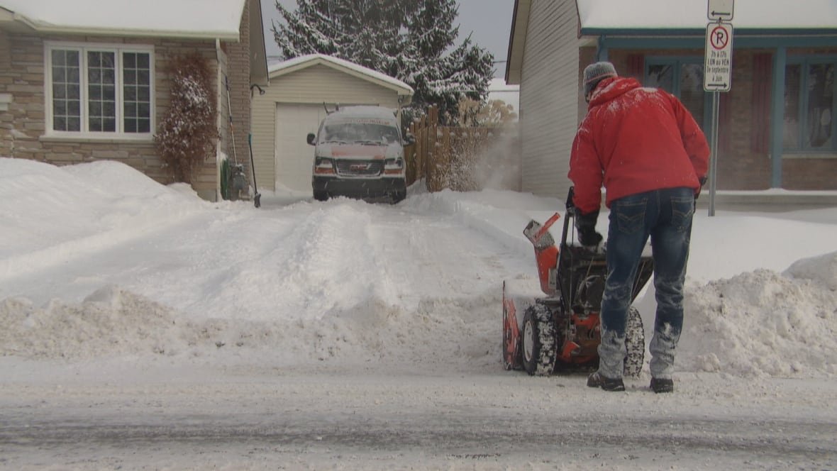 gatineau-ottawa-snow-weather-winter-blower-cleanup Someone in a red winter jacket works a snowblower on a driveway.