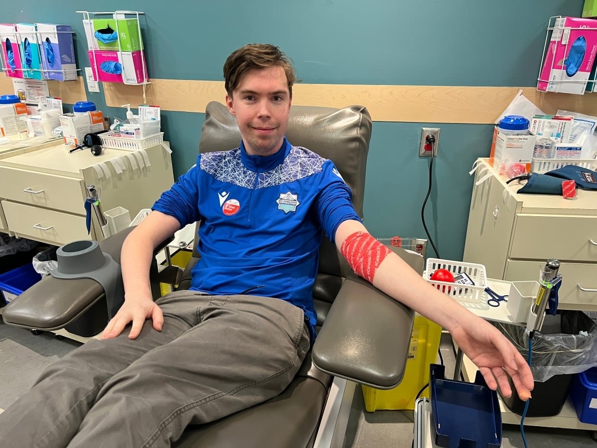 jack-mol A man in a blue shirt sitting in a chair with red medical tape around his arm after donating blood.