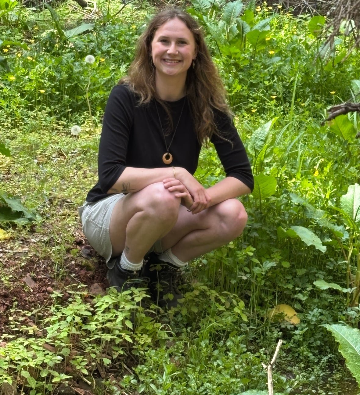 julie-goodwin-1 A woman crouching in a green garden surrounded by plants and foliage.