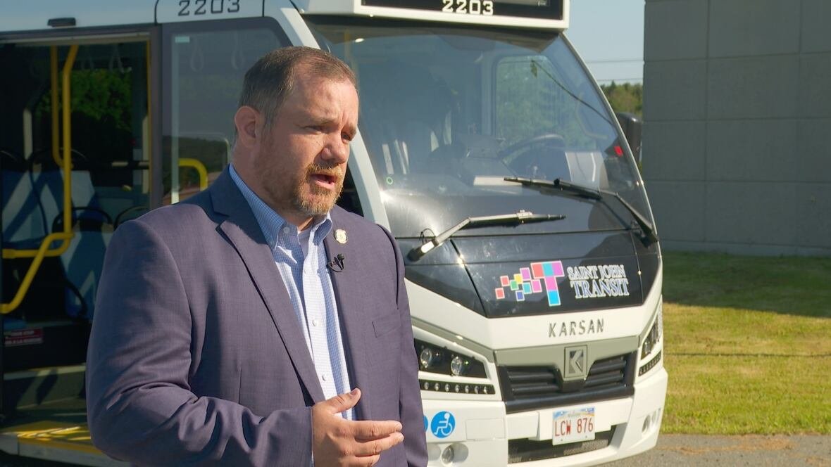 kevin-loughery Man in a shirt and blue blazer standing in front of a flat-nosed bus.