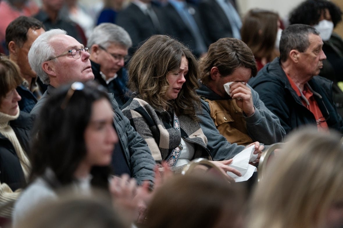 Several people are seen crying and wiping away tears while seated.