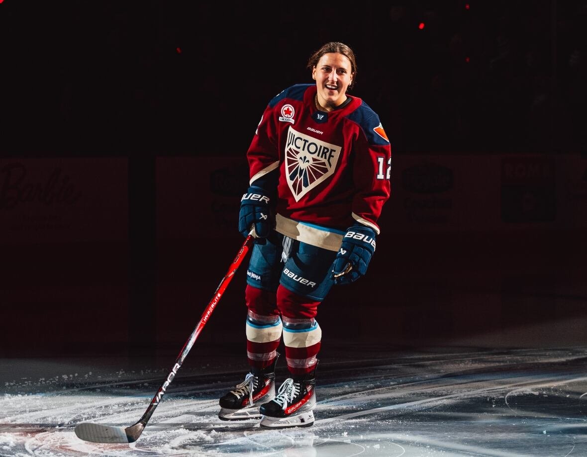 ottawa-charge-v-victoire-de-montreal A hockey player wearing a red Montreal Victoire PWHL sweater and no helmet smiles on the ice.
