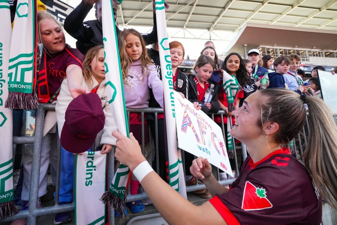 soc-nsl-montreal-toronto-20250419-1 A female soccer player smiles while greeting young female fans near a barricade at a stadium.