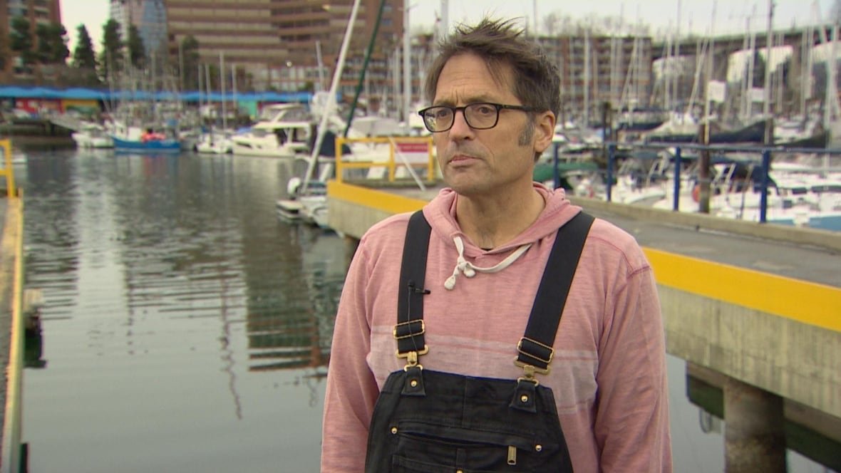 stephen-paetkau A man wearing a pink sweater and overalls is seen in front of a creek-like water body.