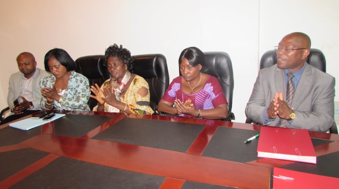 tawembi-ngo-meeting Five people sit at a table with their hands together, as if they are clapping.