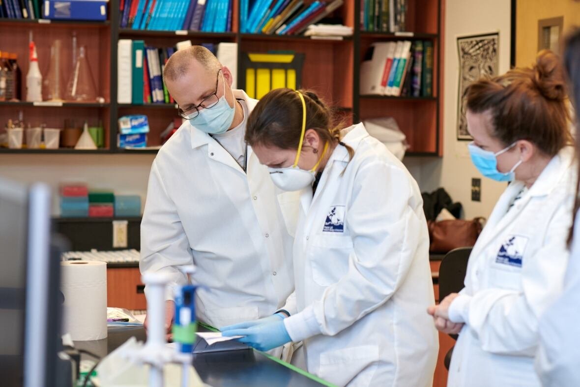 timothy-fraiser Three people on lab coats looking at sample.
