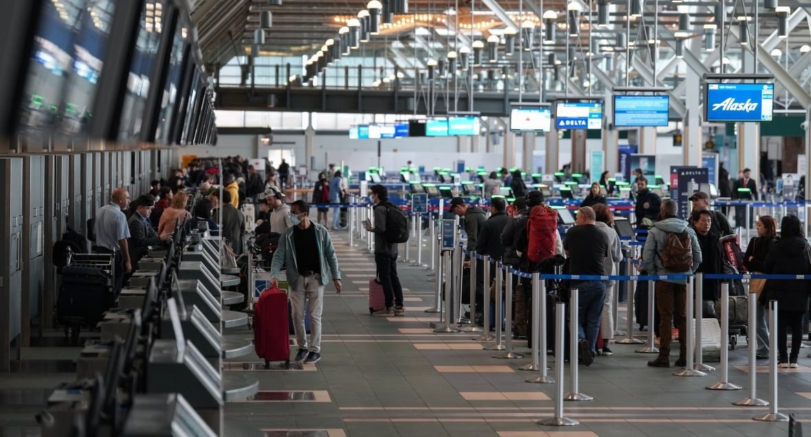 wea-bc-storm-20221226 An airport is seen in this photo, which shows screens at the left side and people lined up at the right.