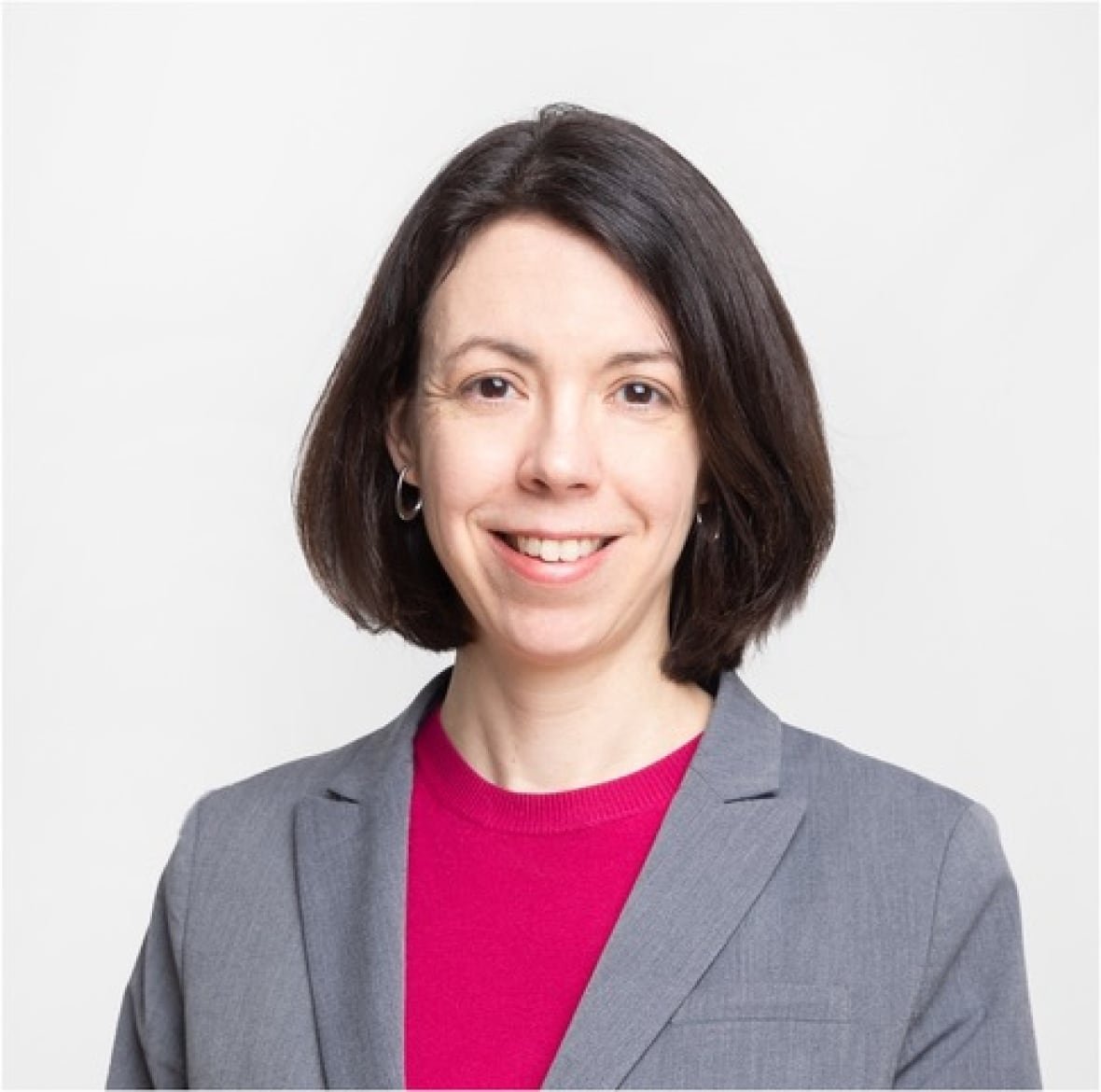 dr-karina-top-measles-infectious-disease-specialist-alberta A woman with chin-length brown hair, and wearing a grey blazer and bright pink shirt, is smiling at the camera.