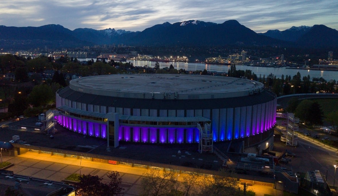 pacific-coliseum-vancouver An arena in Vancouver is shown lit up at night, with the mountains in the background.