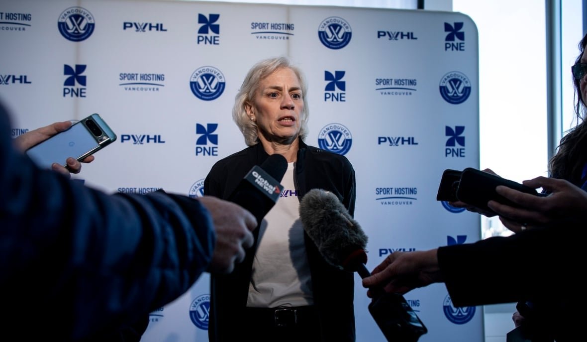 pwhl A woman answers questions from reporters in front of a banner with the PWHL Vancouver logo on it.