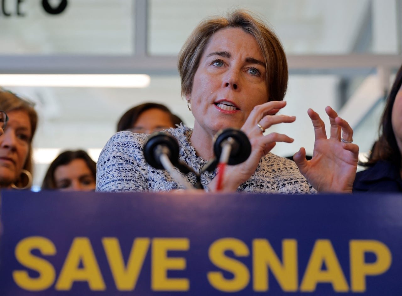 A woman gesturing while speaking at a podium with a placard reading, "Save Snap."