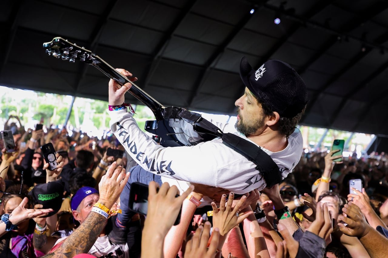 A guitarist crowd-surfing and playing guitar during a live show.