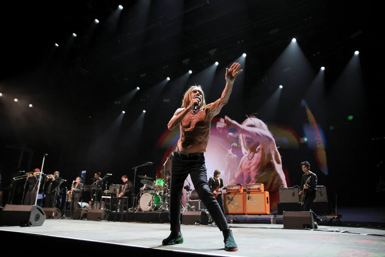 A male singer without shirt performing on a stage with band members in the background.