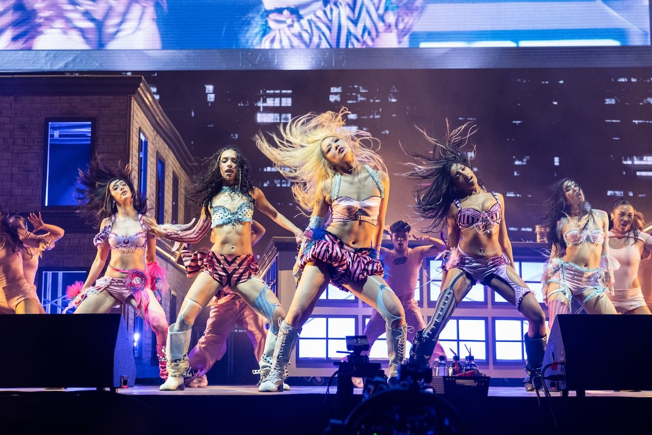 An all-female band performing on stage with backup musicians in the background.
