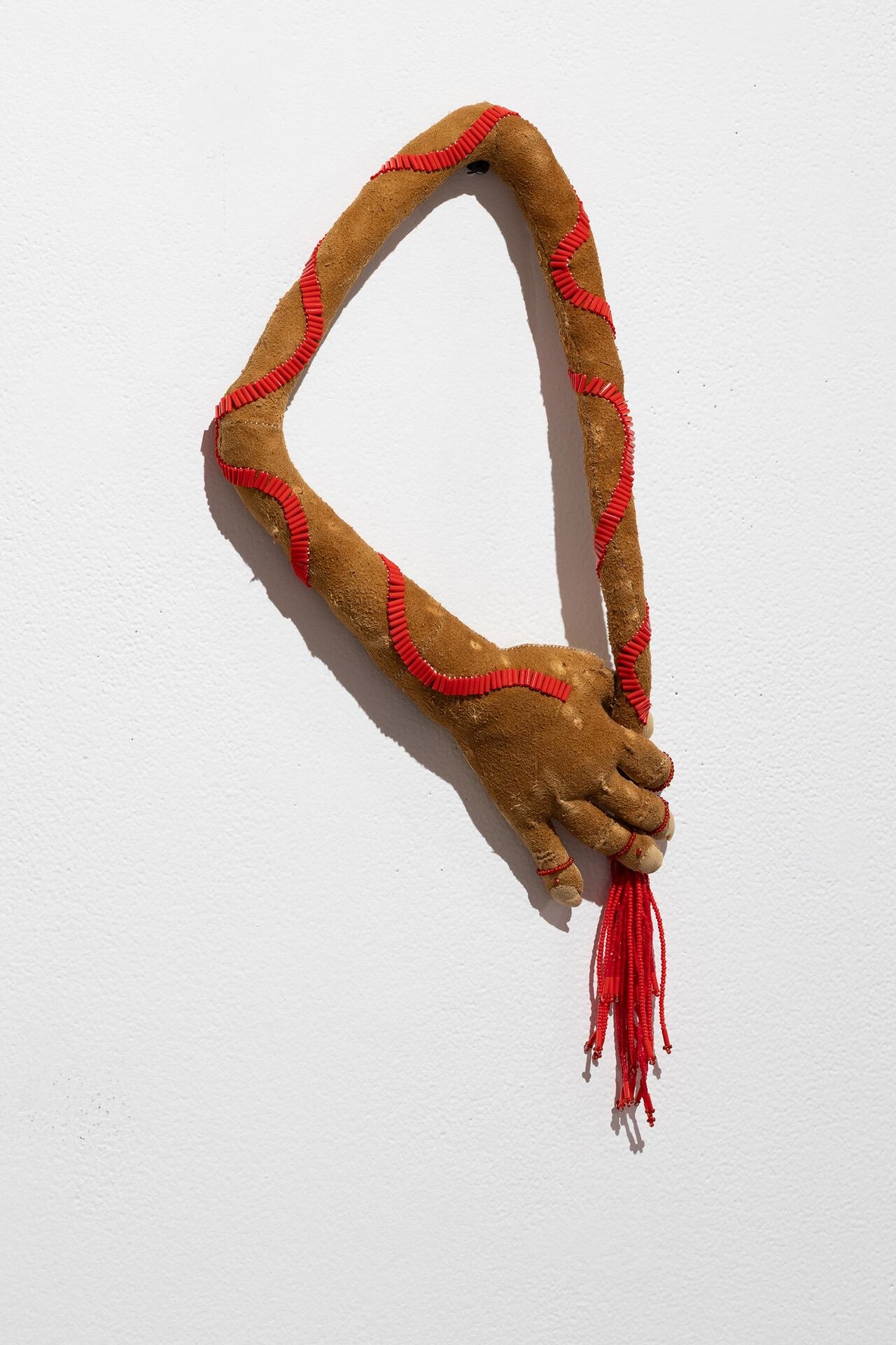 Artwork featuring a hand and arm bending around to itself, made of caribou hide, beaver fur, and beads.
