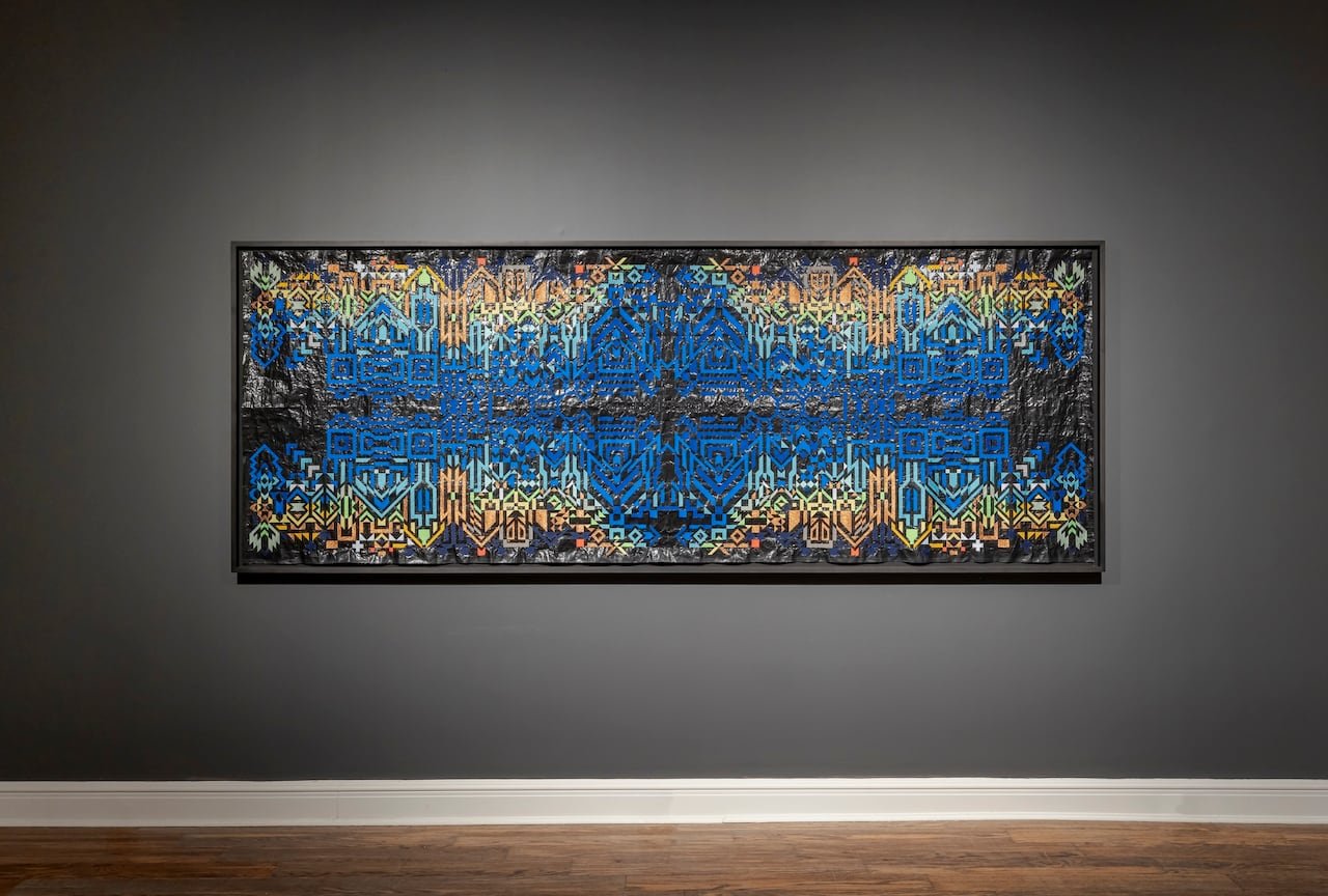 Large blue and gold embroidery hanging on a gallery wall.