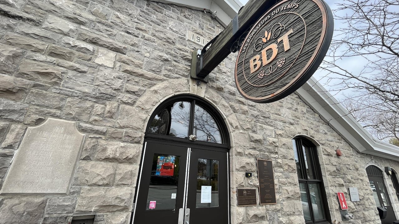 A close-up of a stone building with a brewery's logo attached to a wooden sign.