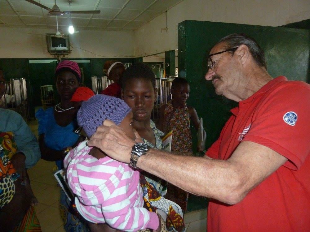 default-19062 A senior Canadian man putting a knit cap on a Ghanaian baby.