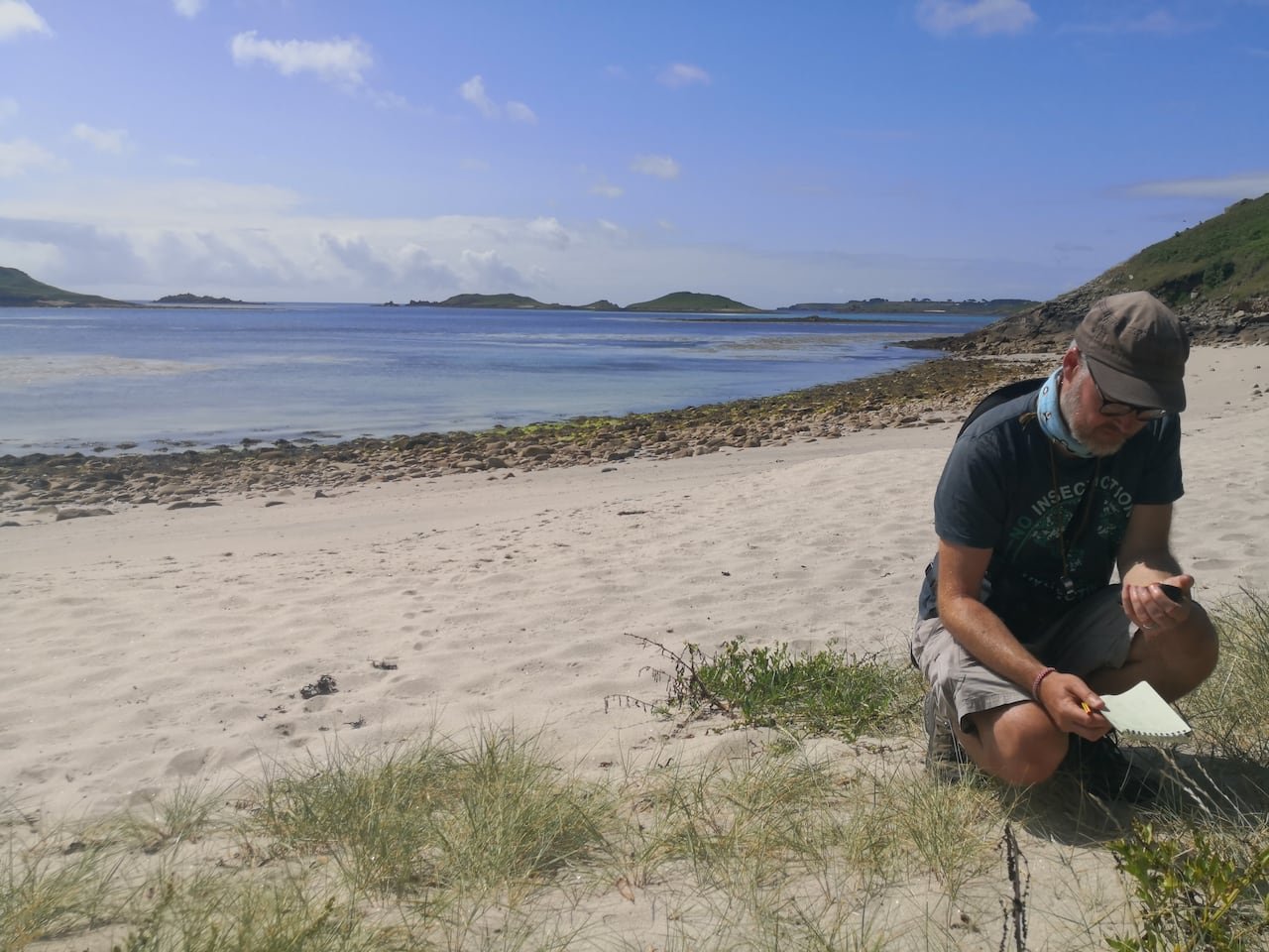 default-3417 Man crouched on a beach writing in a notebook