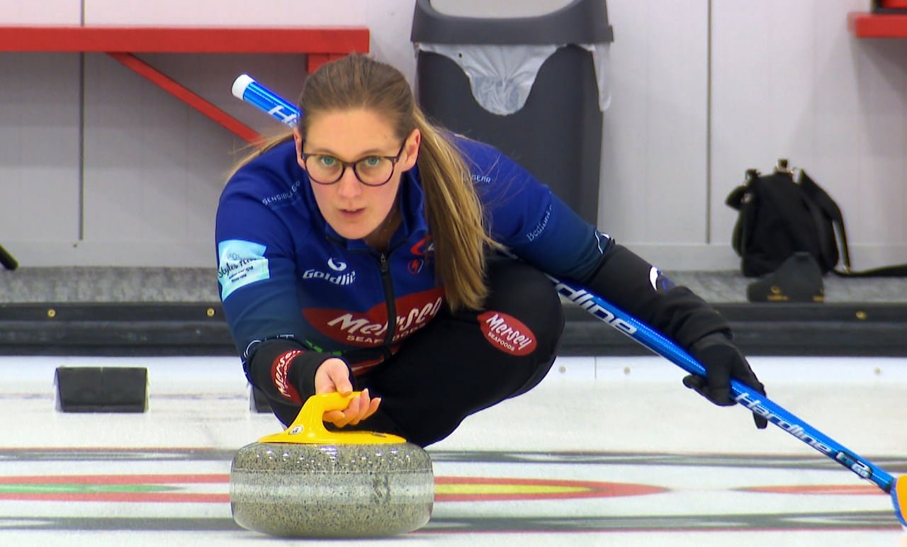 A curler with glasses and a ponytail slides down the ice during a match.