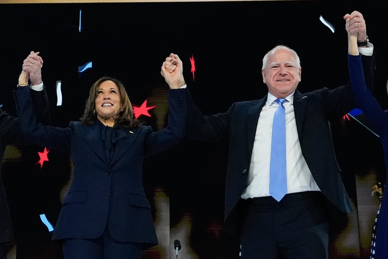A man and a woman in suits raise their hands together on stage.