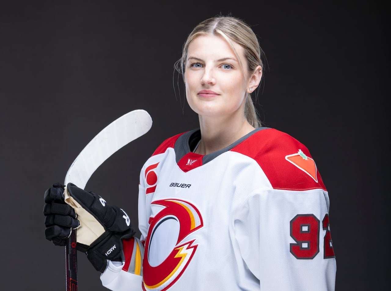 default-9250 A women's hockey player wearing a jersey with a white base, with red shoulder patches, yellow, red, and light grey striping and the team's "O" logo prominently displayed on the front.