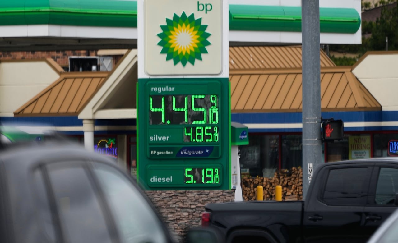 A gas station sign can be seen between vehicles showing a price of $4.45 9/10 for regular and $5.19 9/10 for diesel.