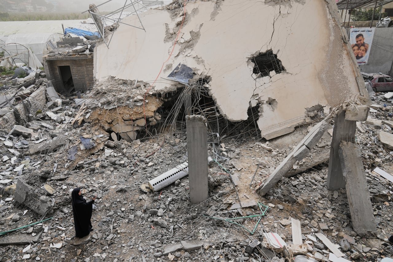 A woman stands next to a destroyed building surrounded by rubble.