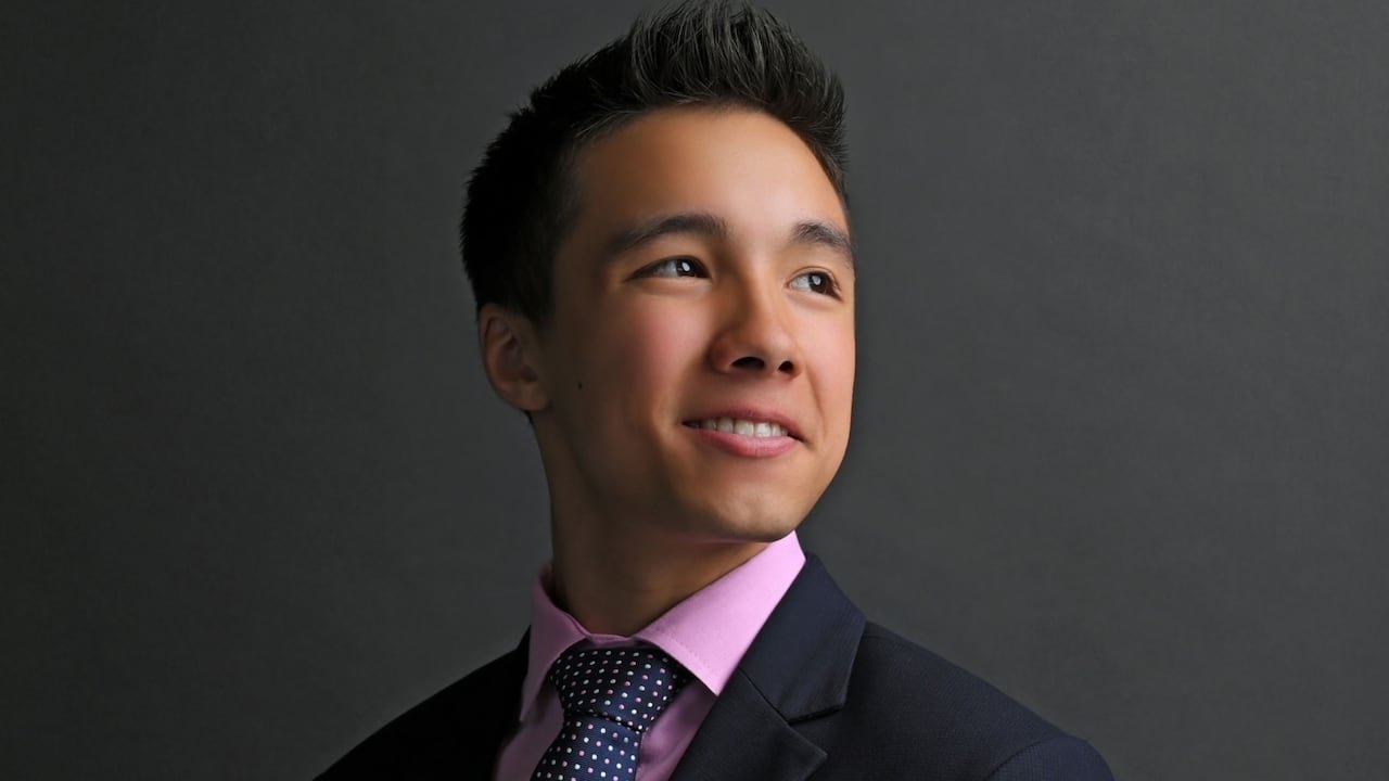 default-22 A young man wears a suit and smiles off to the side.